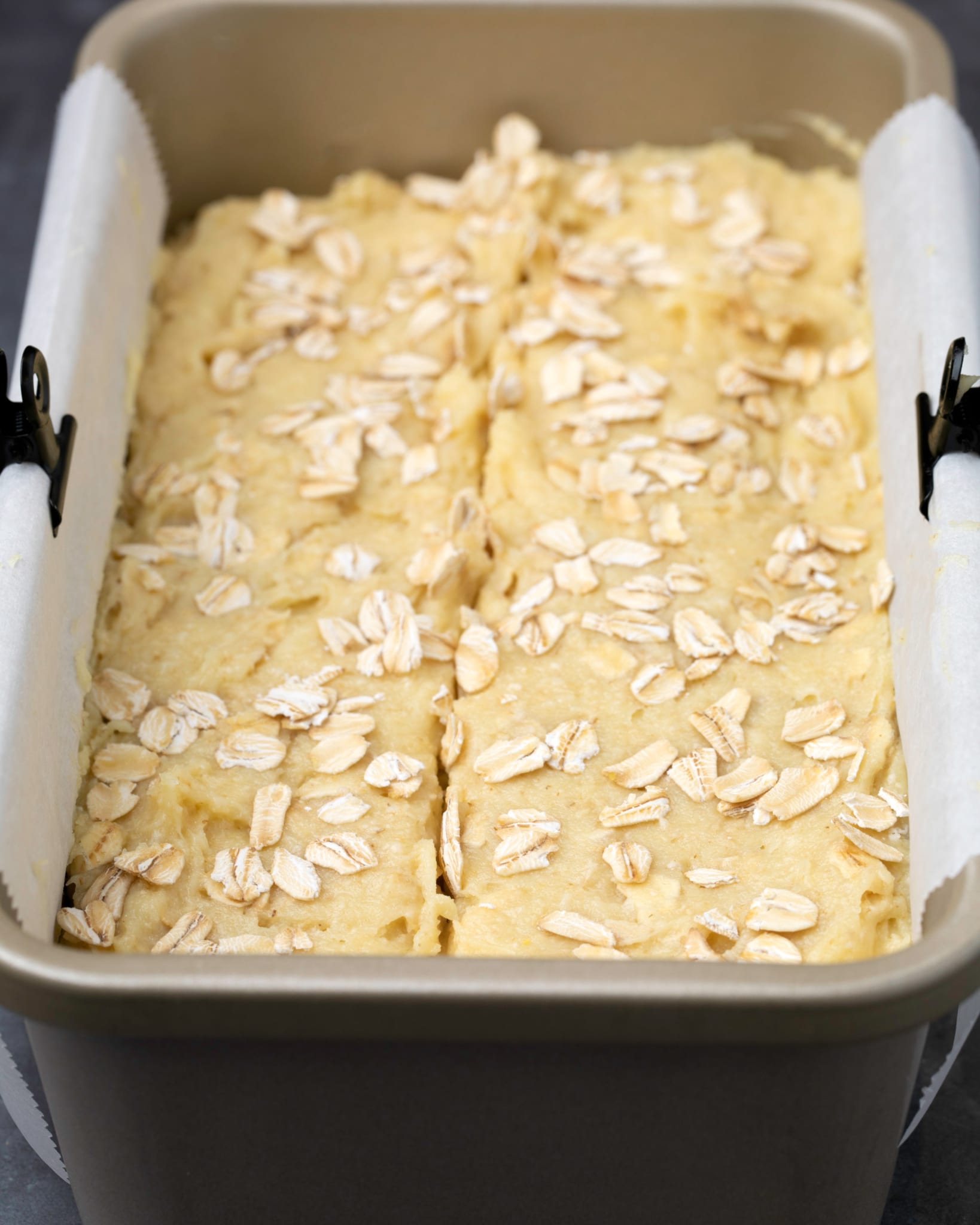 Oat bread batter in loaf pan on white paper with clips