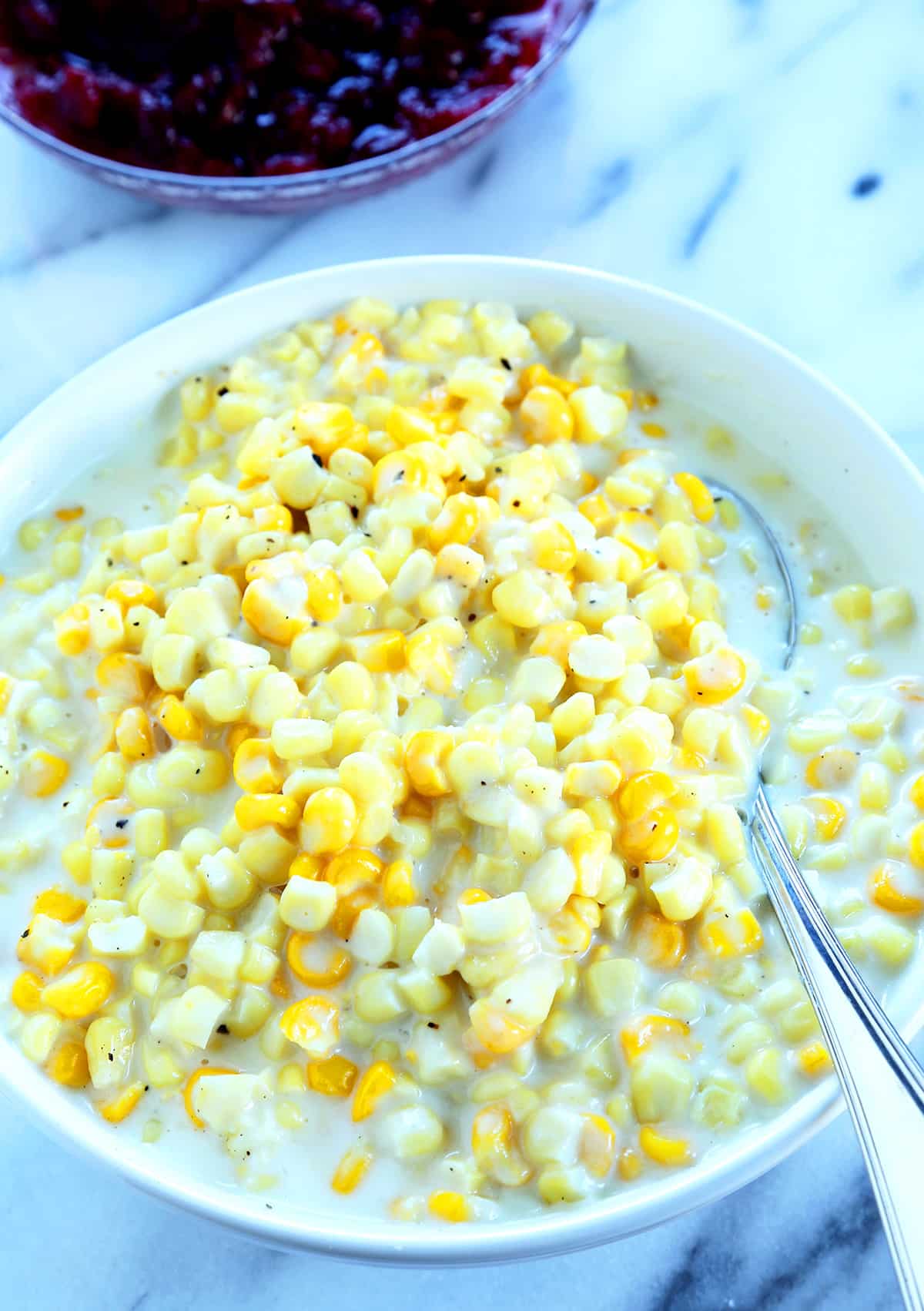 Overhead view off creamed corn in a white bowl with a metal spoon
