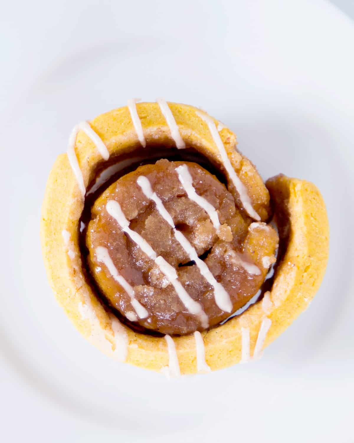 overhead image of a single orange-brown cinnamon roll unfurling with light drizzling of white icing