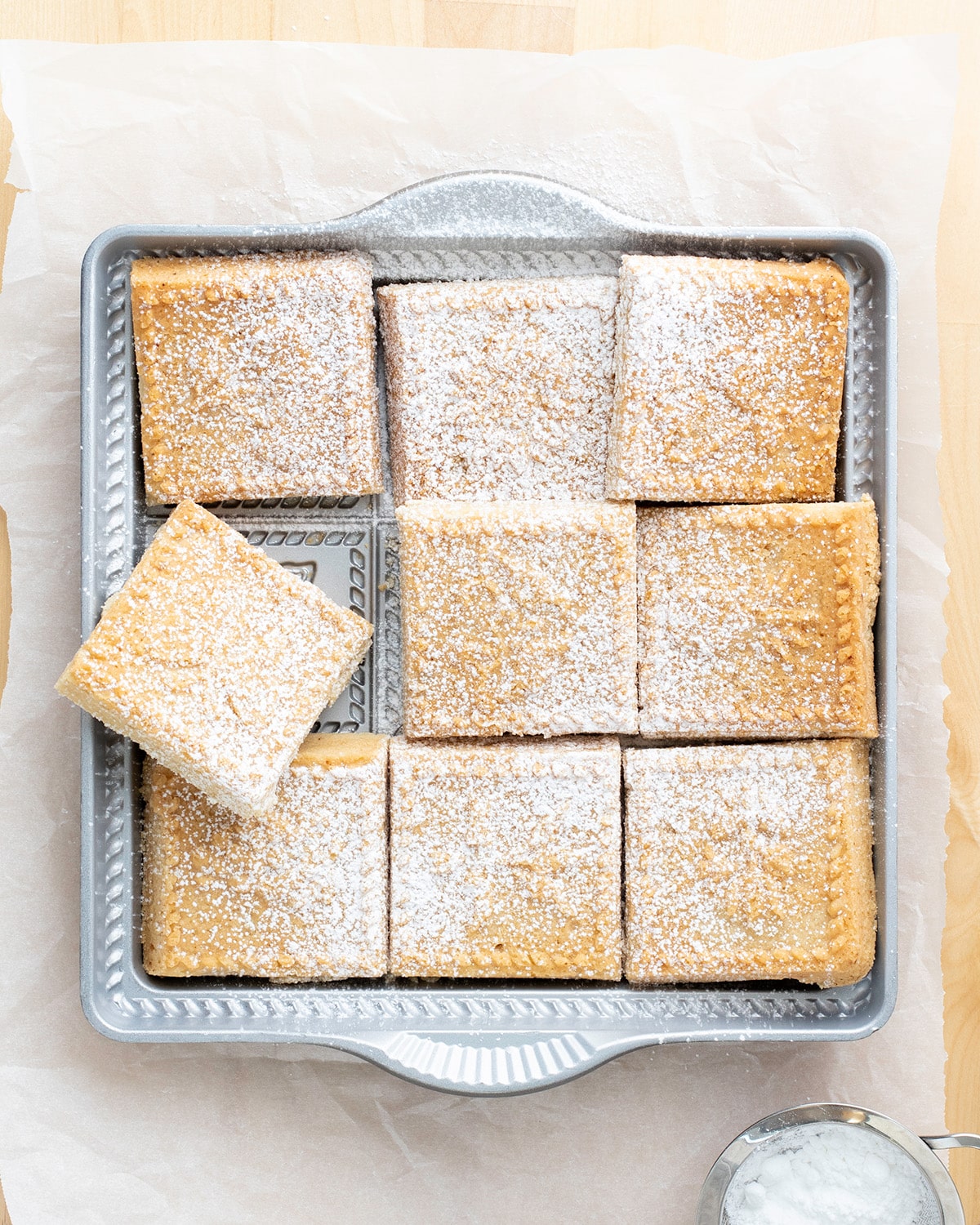 Overhead image of cut shortbread squares in pan with powdered sugar on white paper