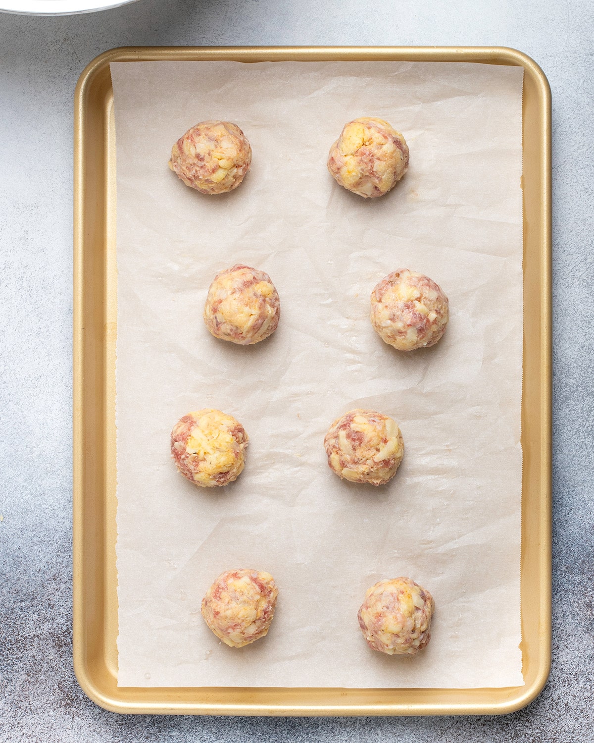 Overhead image of raw sausage balls on white paper on gold baking tray