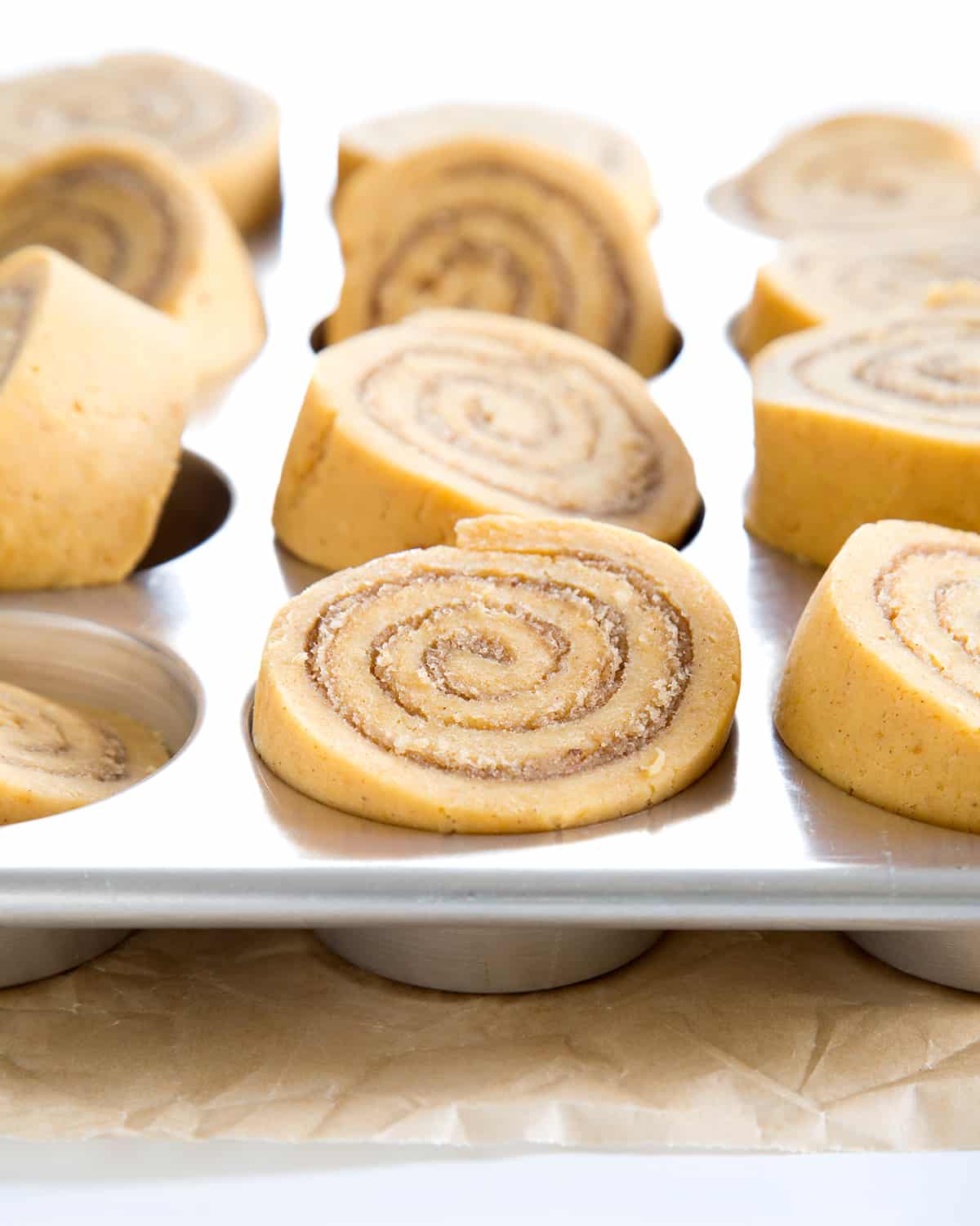 raw shaped pumpkin cinnamon rolls in metal muffin tray