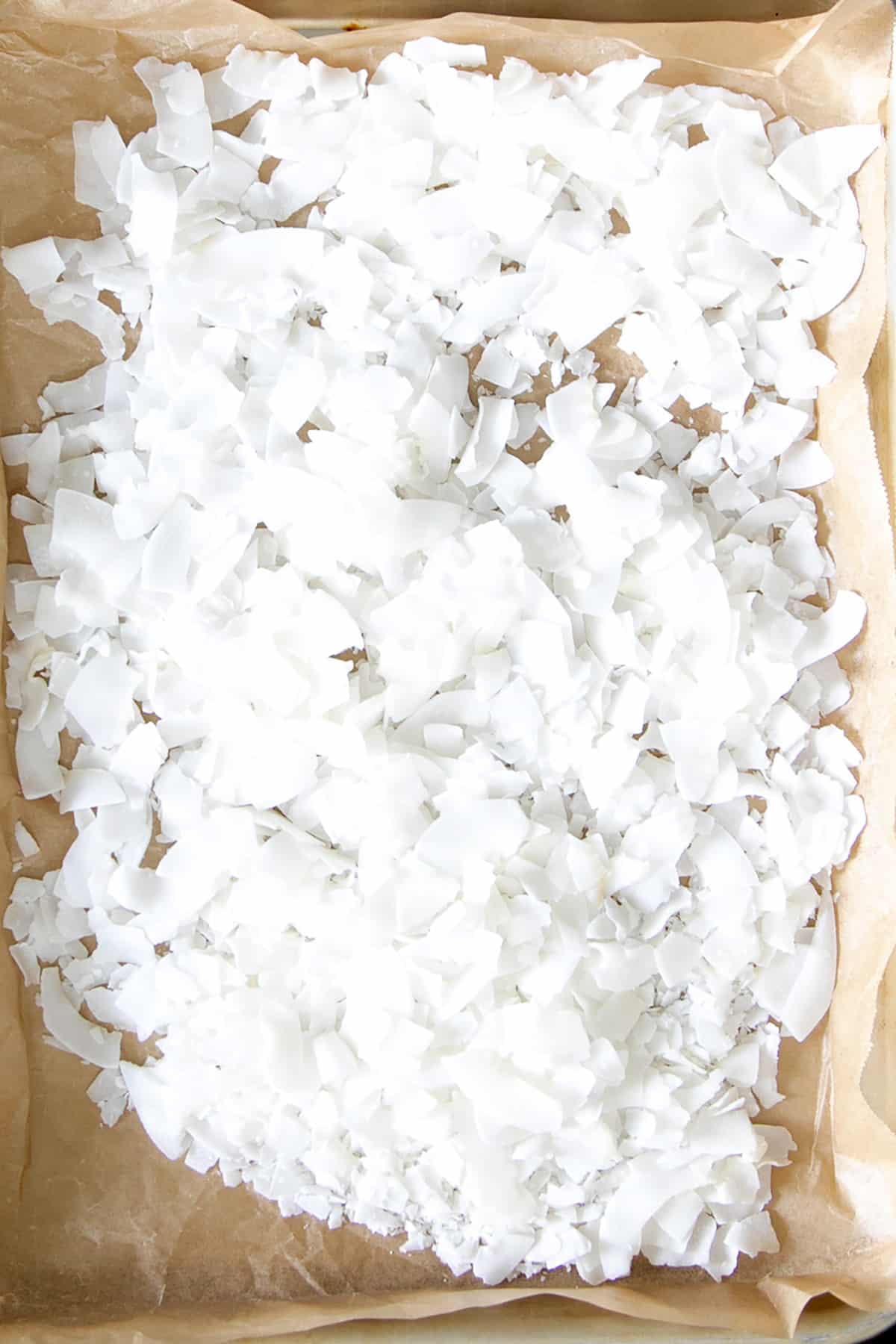 Large white coconut flakes cover a parchment-lined baking sheet.