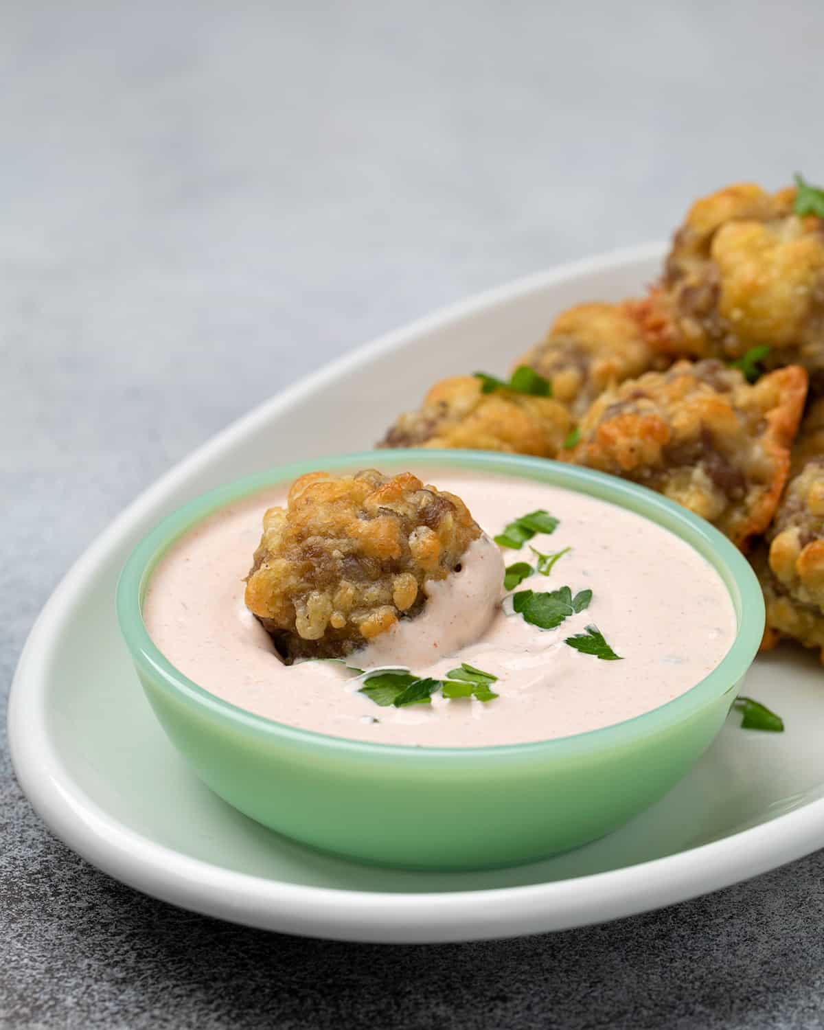 Sausage ball in light orange dipping sauce in small green bowl