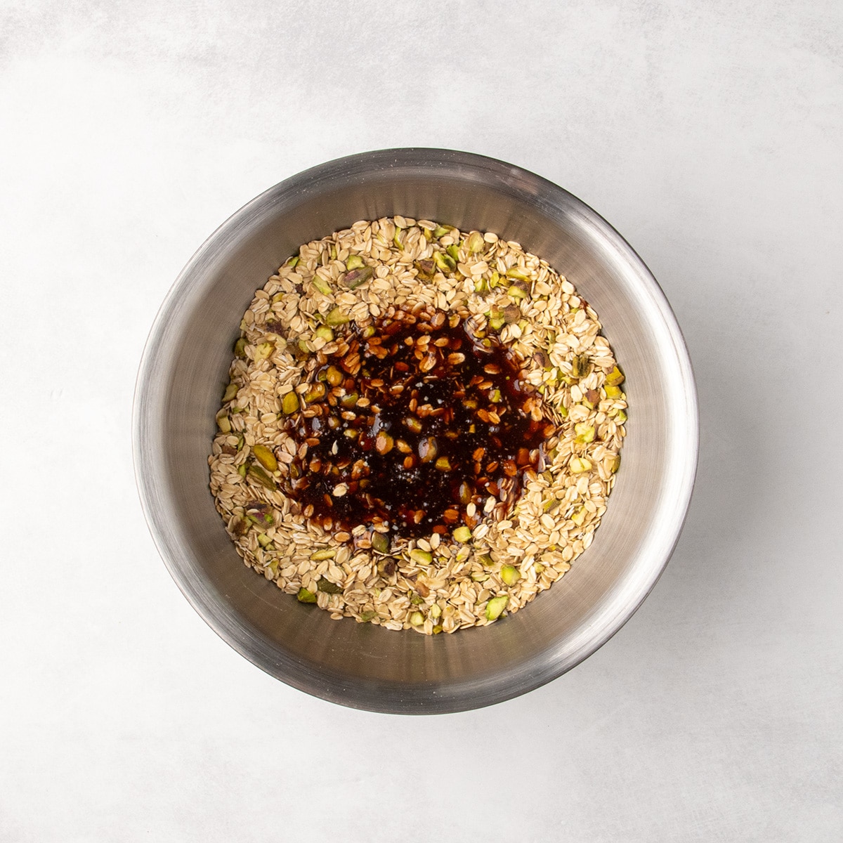 Dark reddish-brown liquid sits in the center of a bowl of oats, pistachios, and seeds.