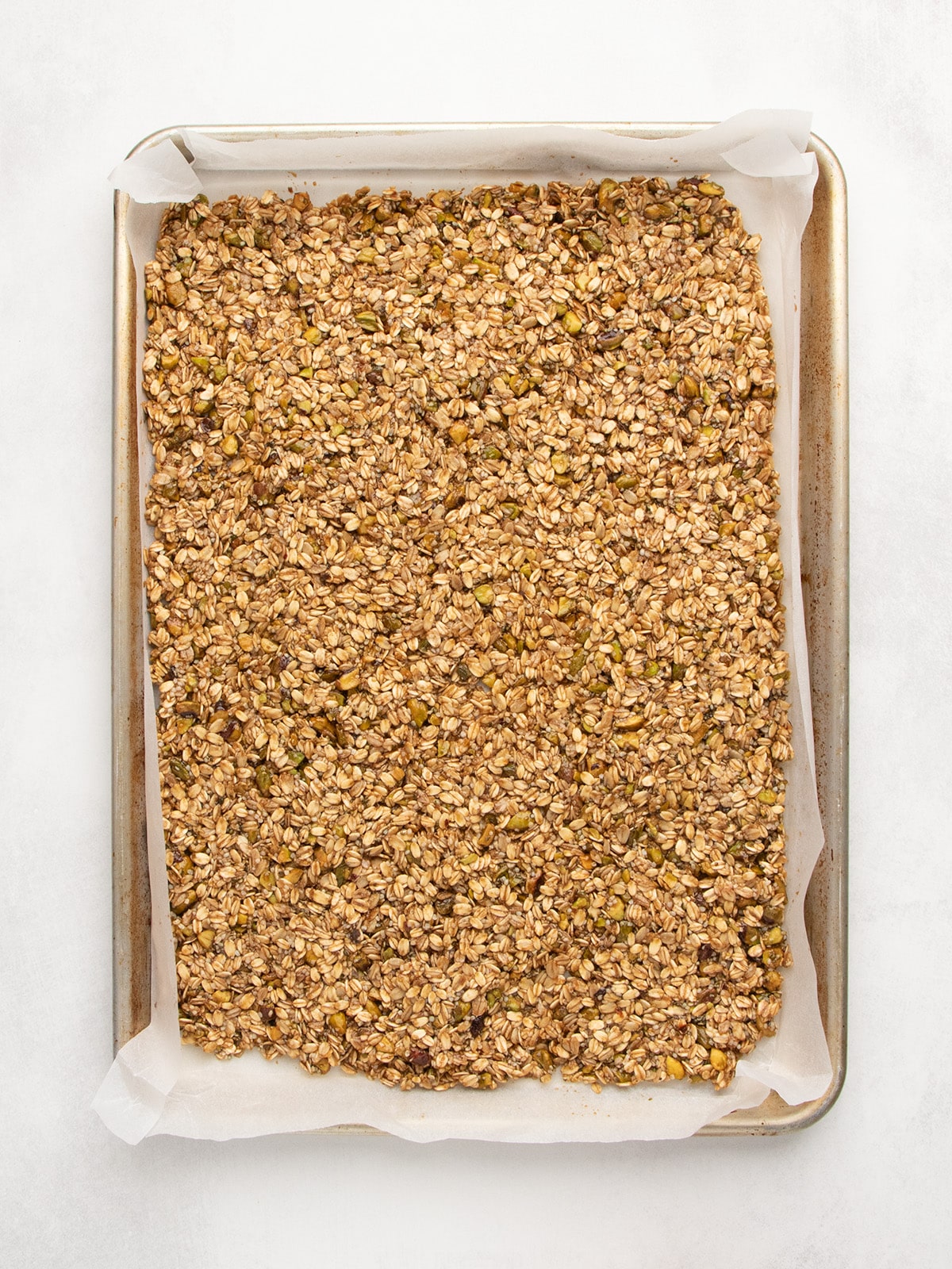The oat and pistachio mixture sits in an even layer on a parchment-lined baking sheet.