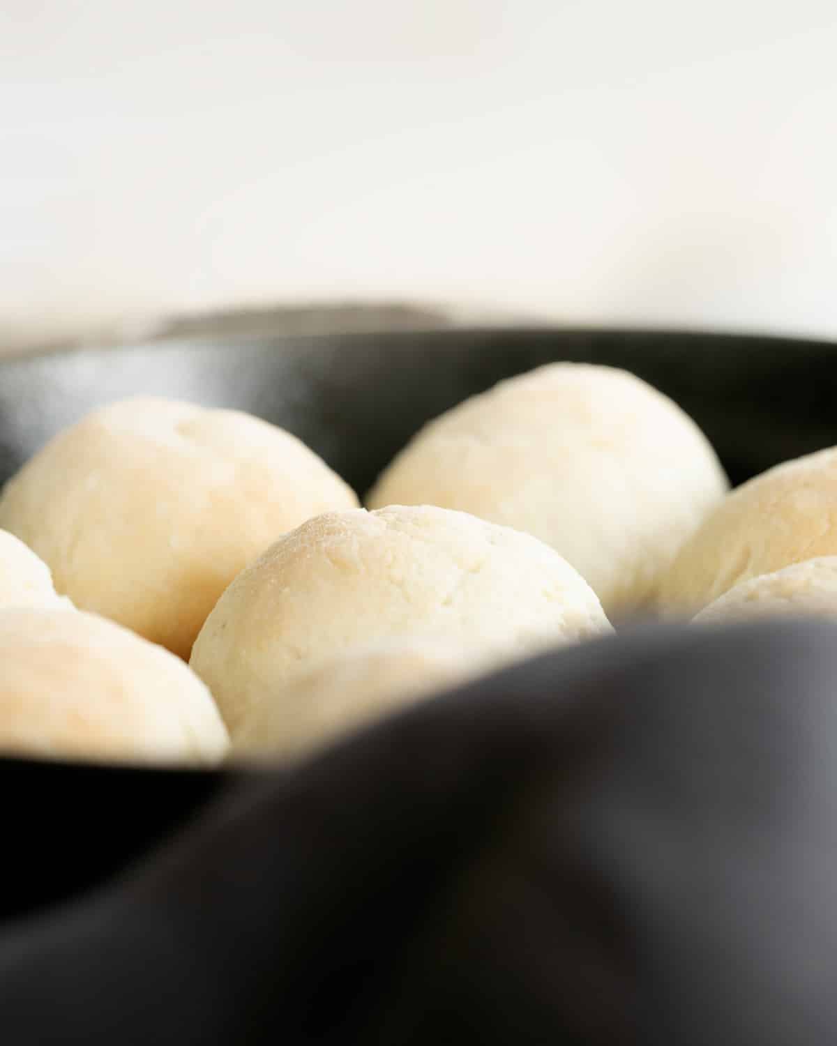 A close-up shows several round dinner rolls with lightly browned tops inside a black cast iron skillet.