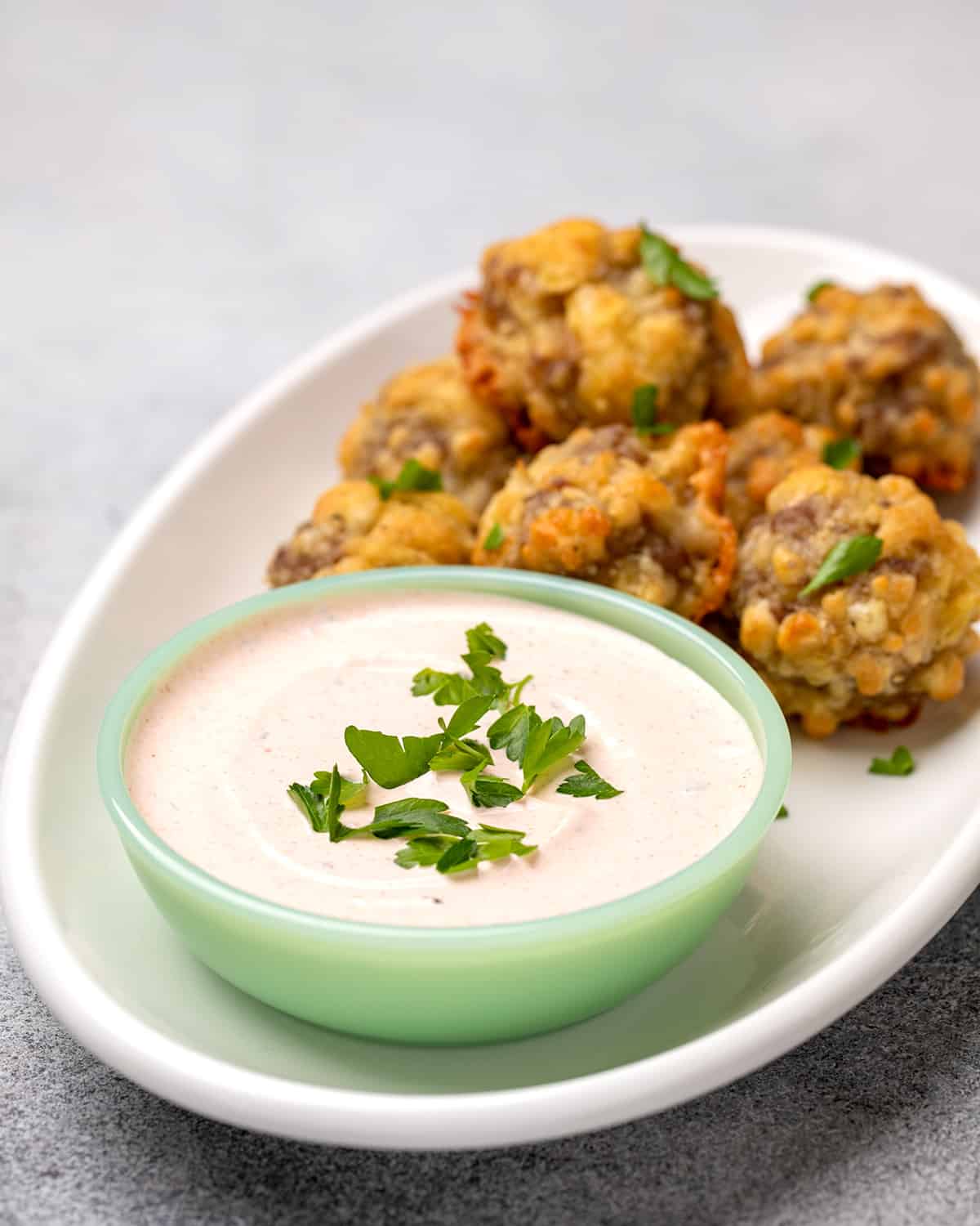 Light orange dipping sauce with fresh parsley in small green bowl with sausage balls on platter