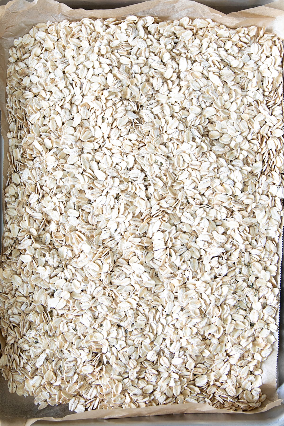 Rolled oats cover a parchment-lined baking sheet.
