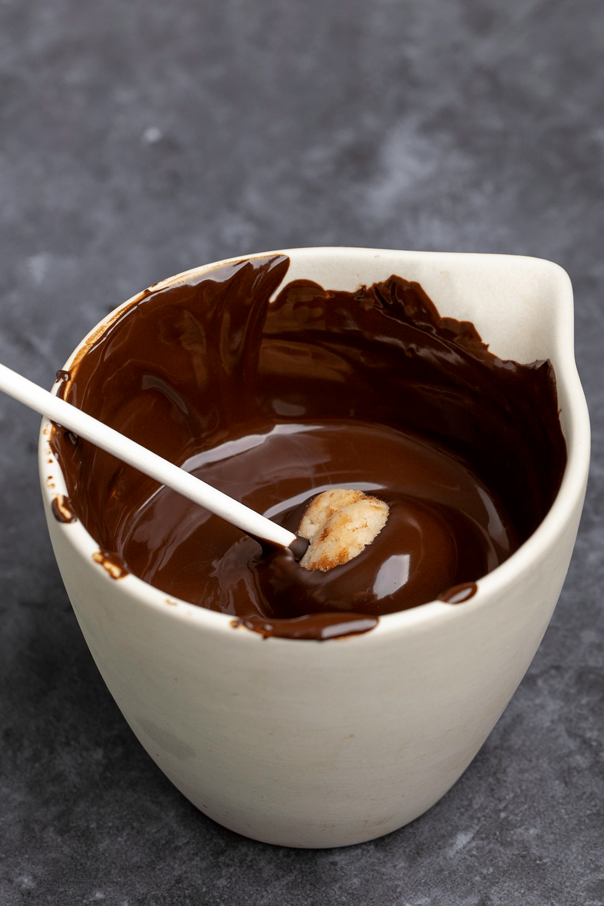 Cake pop on lollipop stick being dipped in melted chocolate