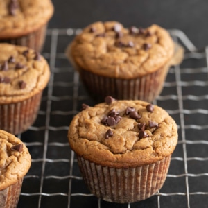 closeup image of brown flourless peanut butter muffin with mini chocolate chips on a wire rack with more muffins in the background