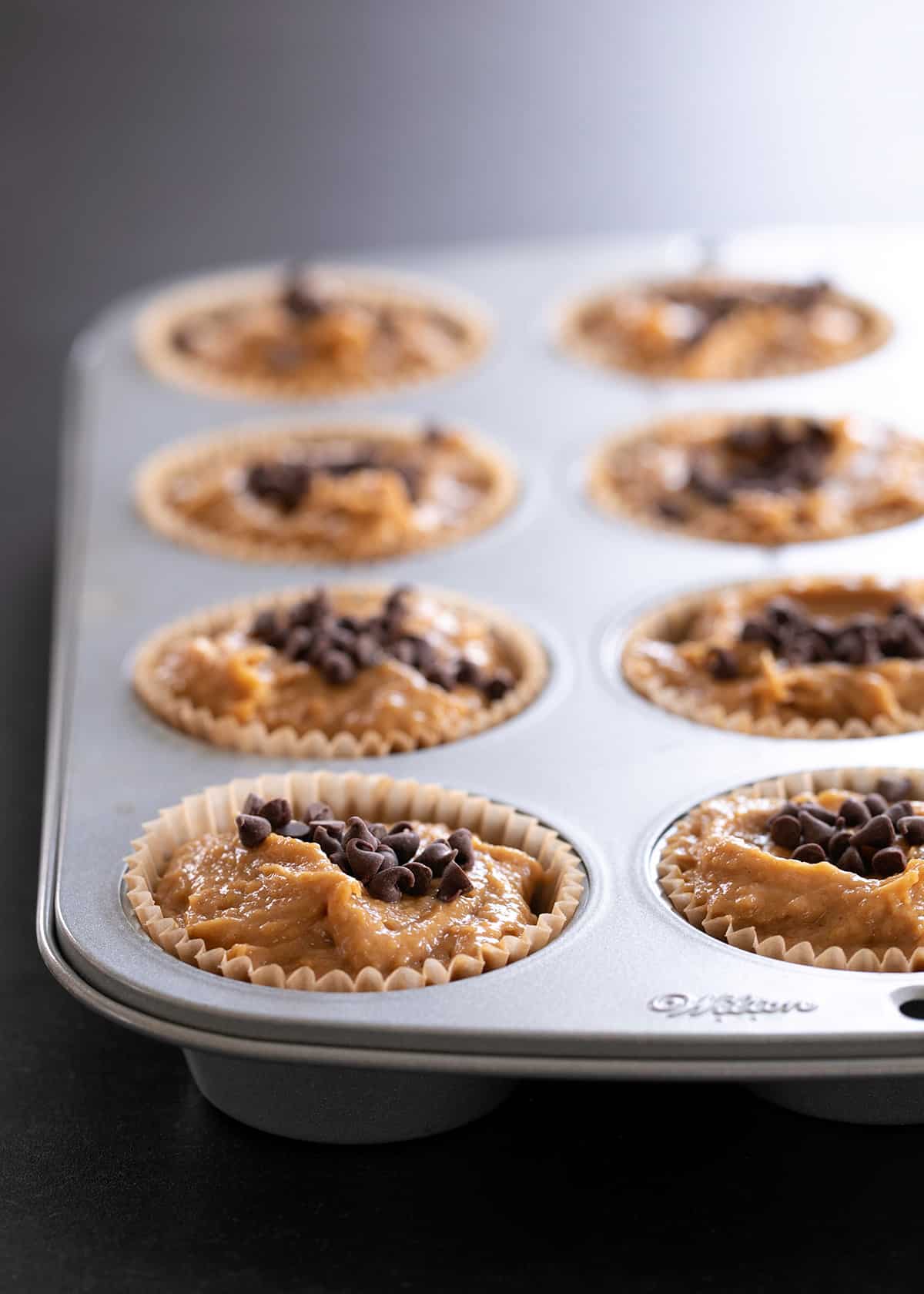 Flourless peanut butter muffins, made with no flour, no banana, and no dairy, pictured raw in the muffin tin, ready for the oven.