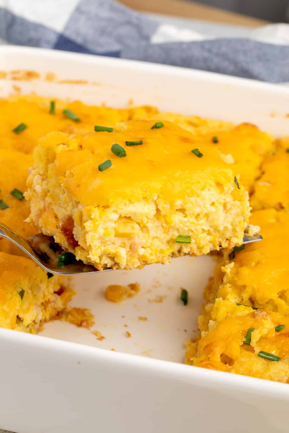 A square of baked corn casserole is lifted from the baking dish on a serving spatula.