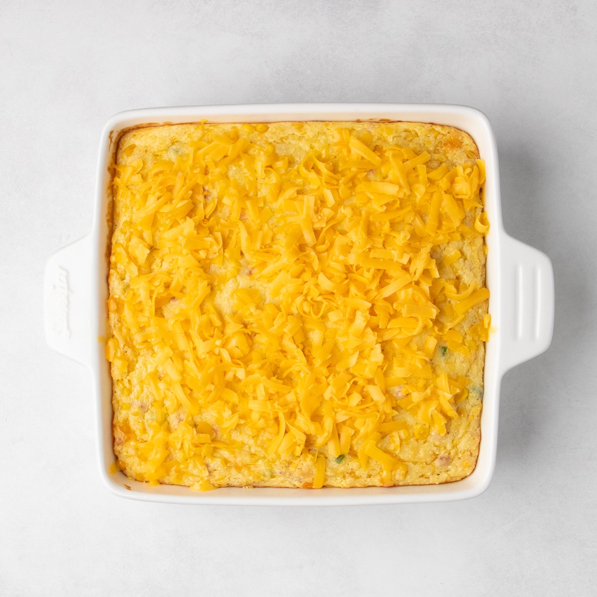 Unmelted shredded yellow cheddar cheese covers the top of the baked corn casserole.