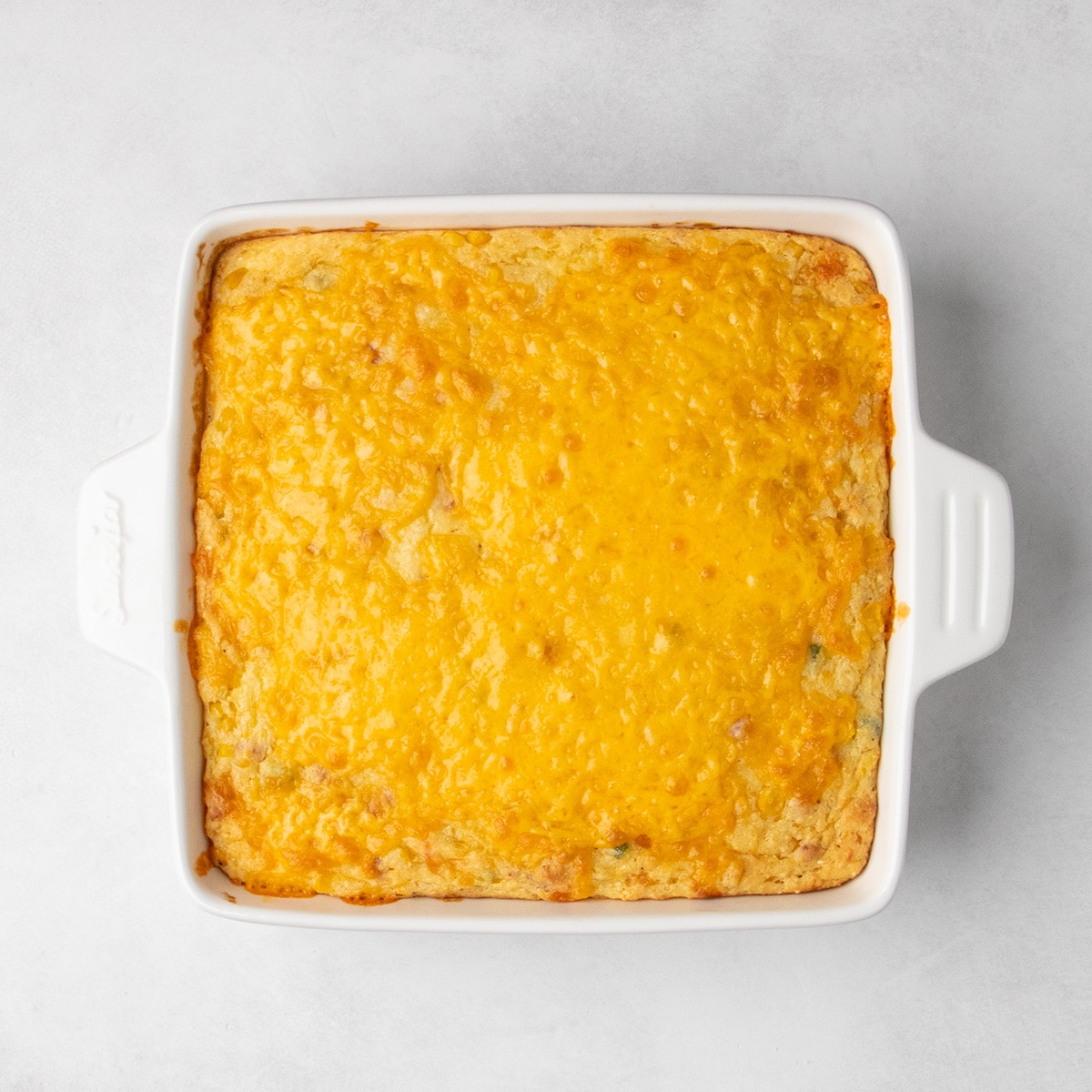 Lightly golden brown melted cheddar cheese covers the top of the baked corn casserole.