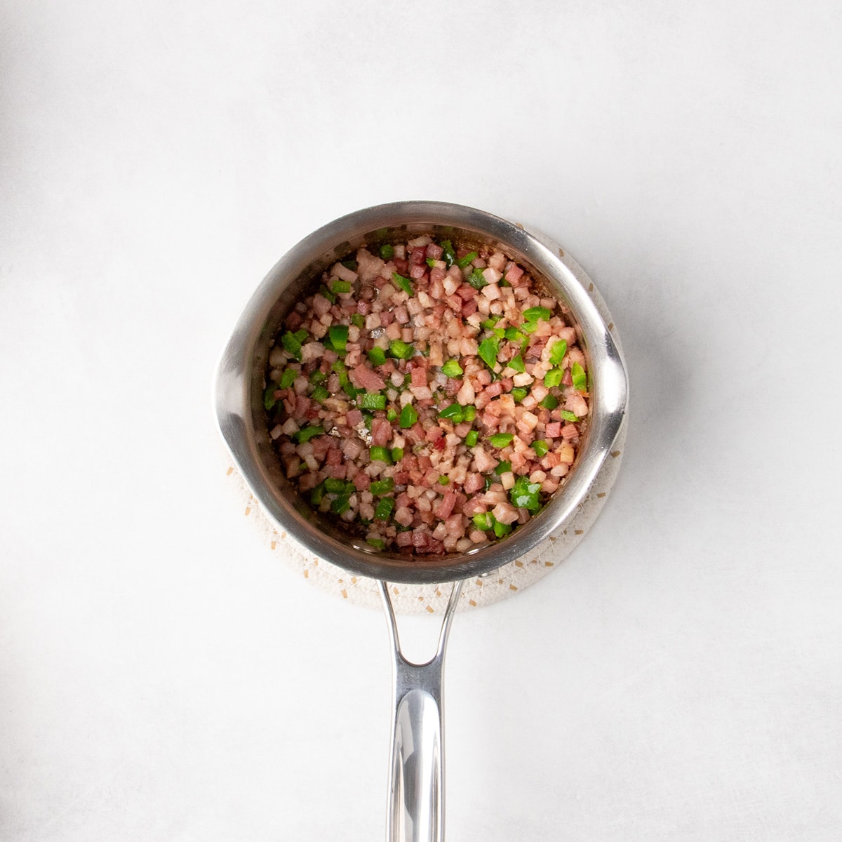 Small cubed pancetta and diced jalapeño peppers cooked together in a small metal saucepan.