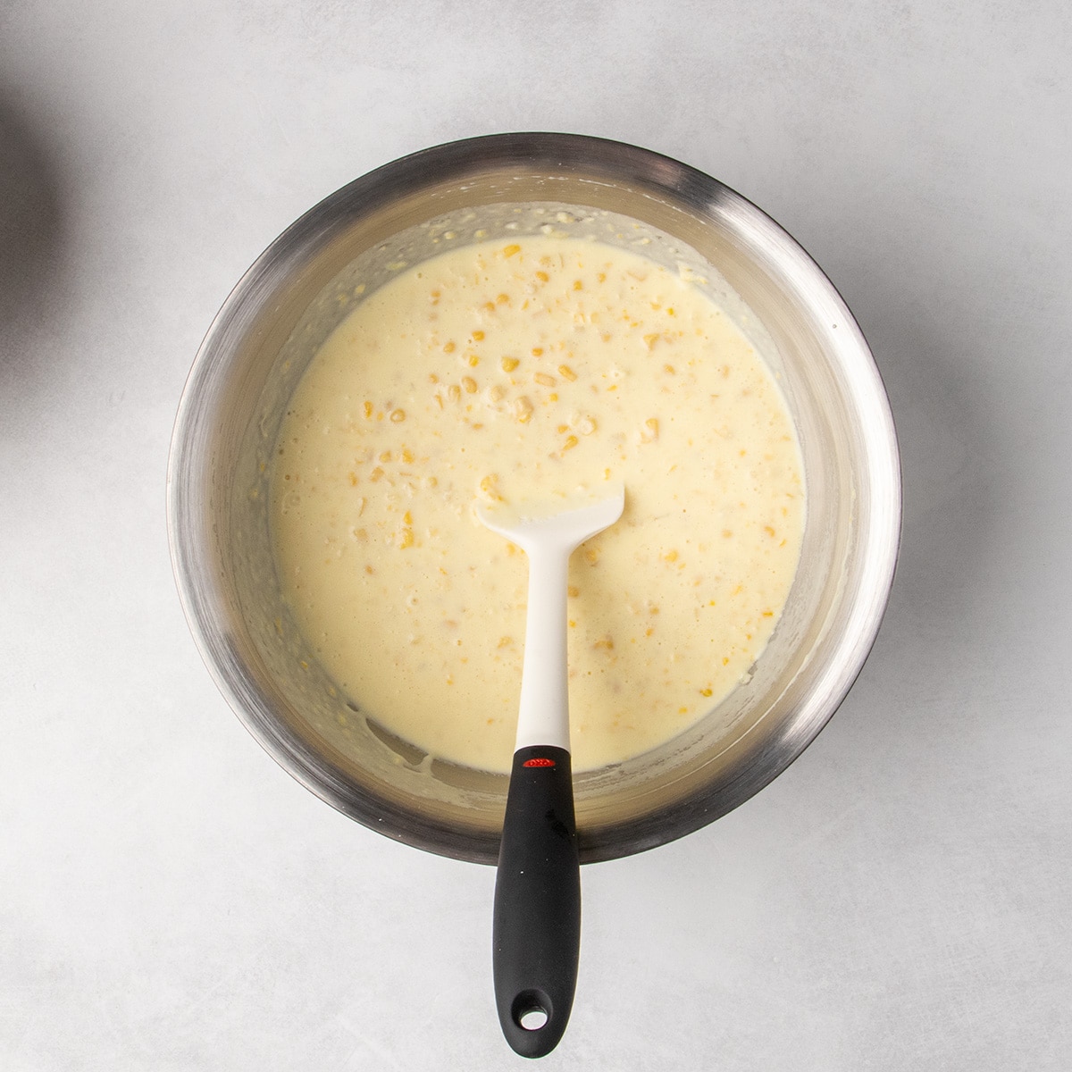 Chopped corn and whole corn kernels mixed into the wet ingredients in a metal bowl.