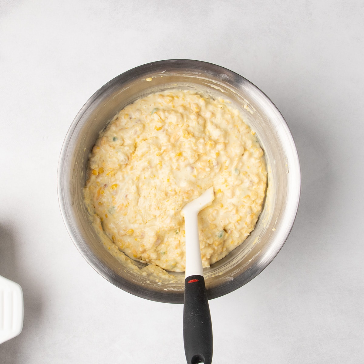 Raw light yellow corn casserole battermixed in a metal bowl with a spatula.