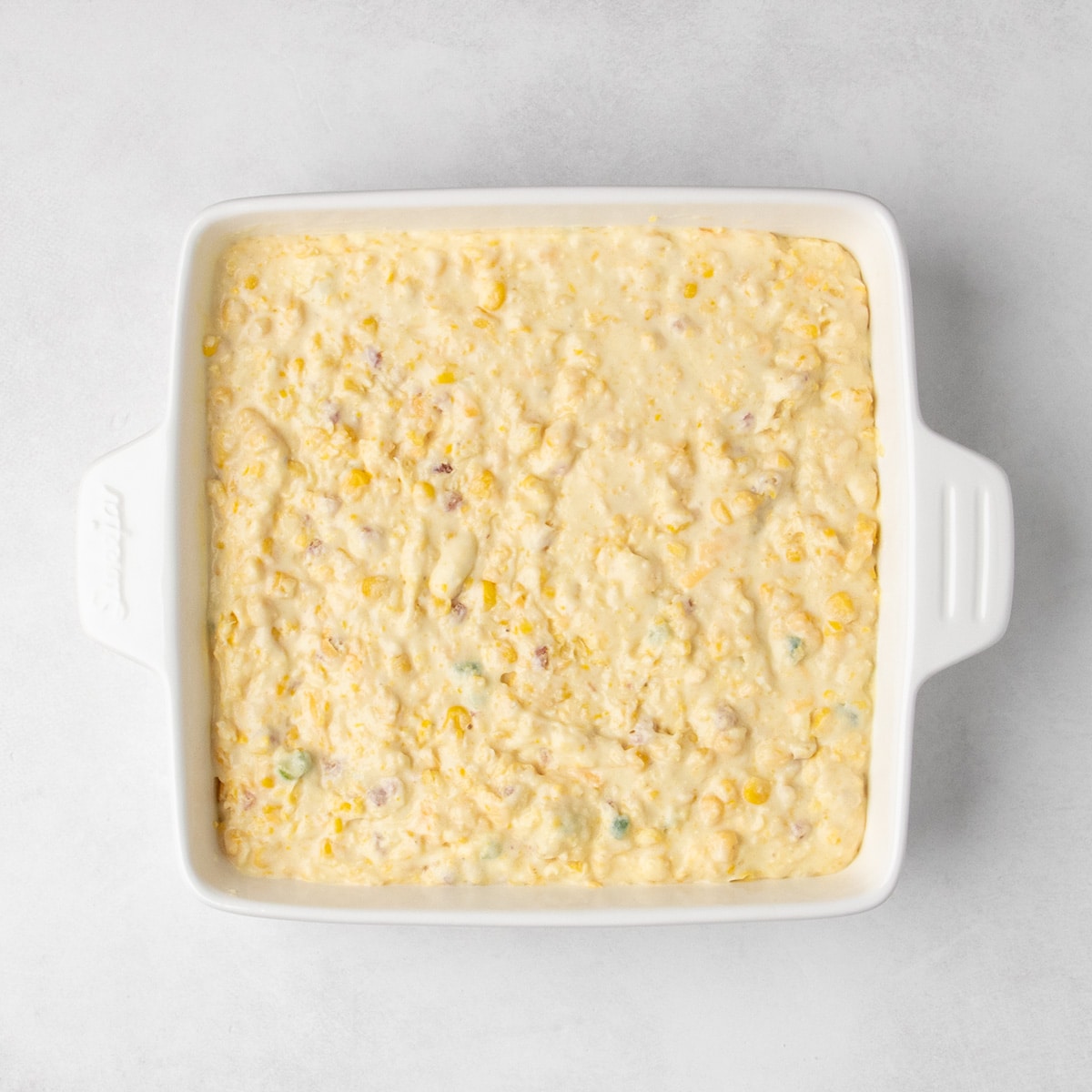 Unbaked corn casserole batter fills a square white baking dish.