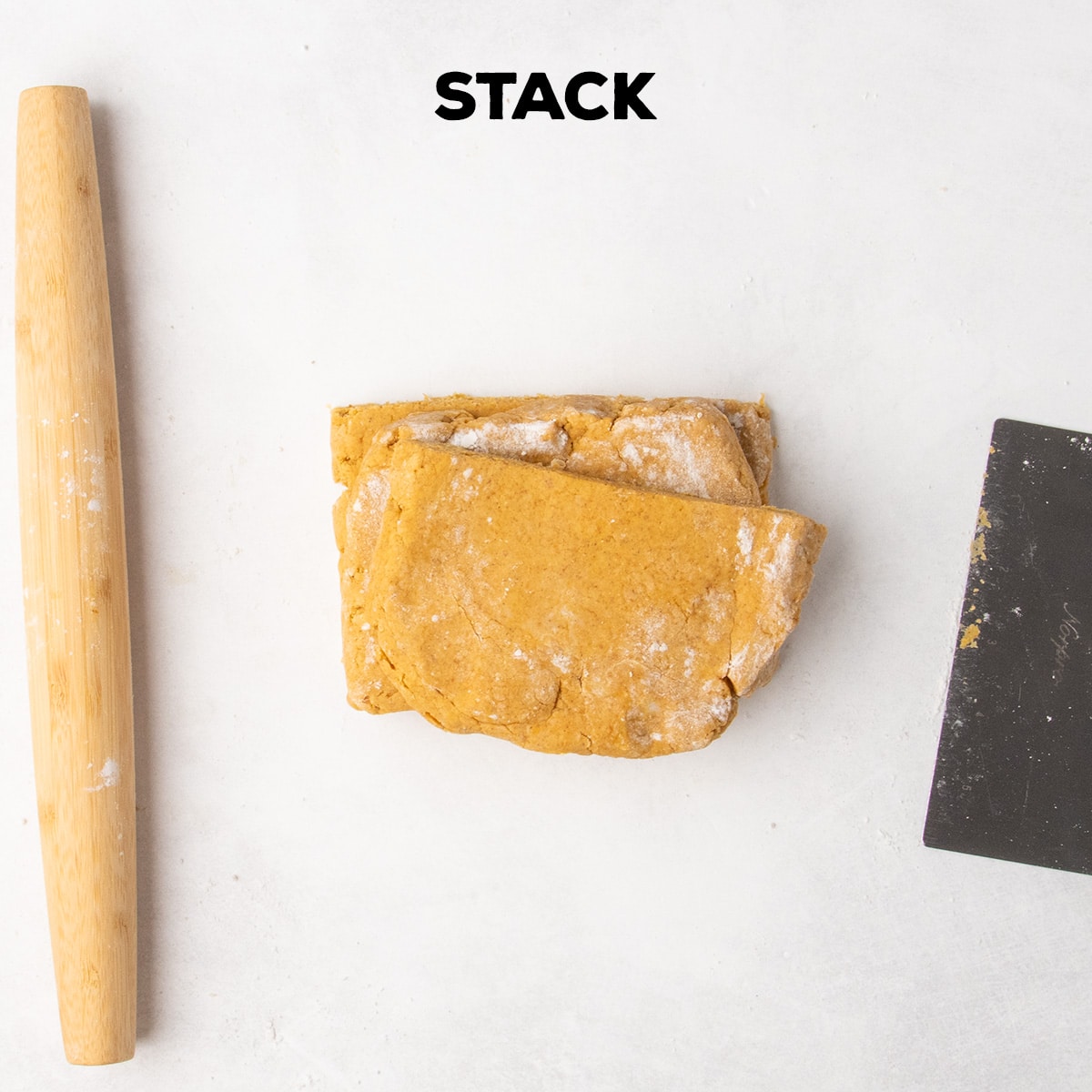 Three sections of orange dough are stacked on a white work surface beside a wooden rolling pin and metal bench scraper beneath the word “STACK.”
