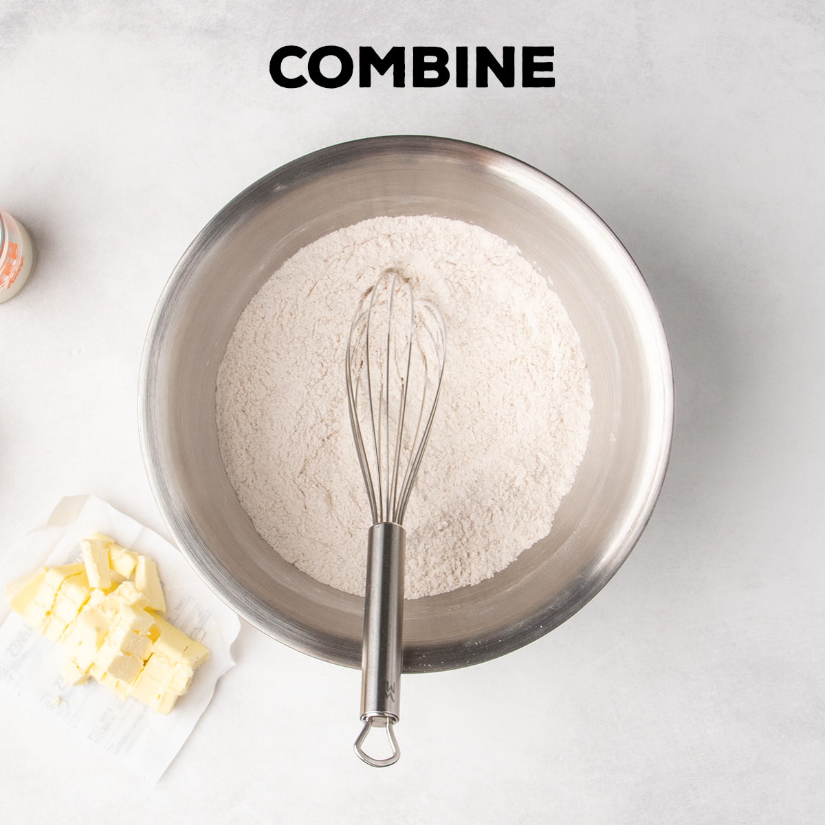 A whisk rests in a metal bowl of combined dry ingredients beneath the word “COMBINE,” with cubed butter beside the bowl.