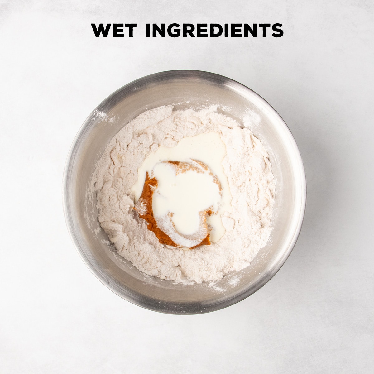 Pumpkin-colored puree and a pale liquid sit in the center of the flour mixture beneath the words “WET INGREDIENTS.”