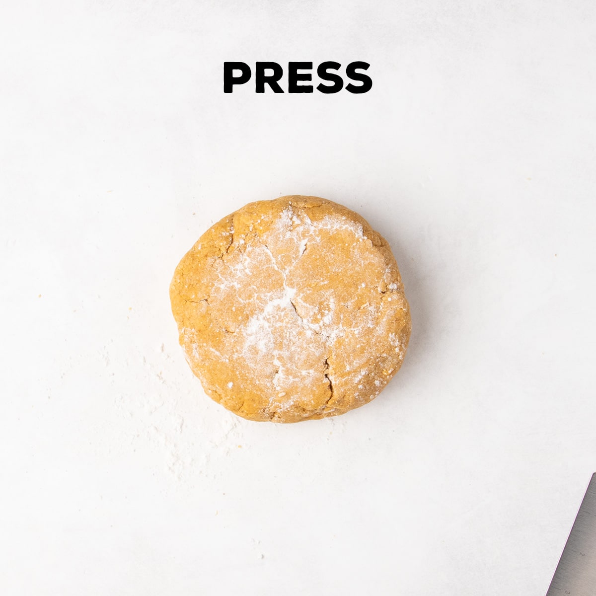 A round mound of orange dough dusted with flour sits on a white work surface beneath the word “PRESS.”
