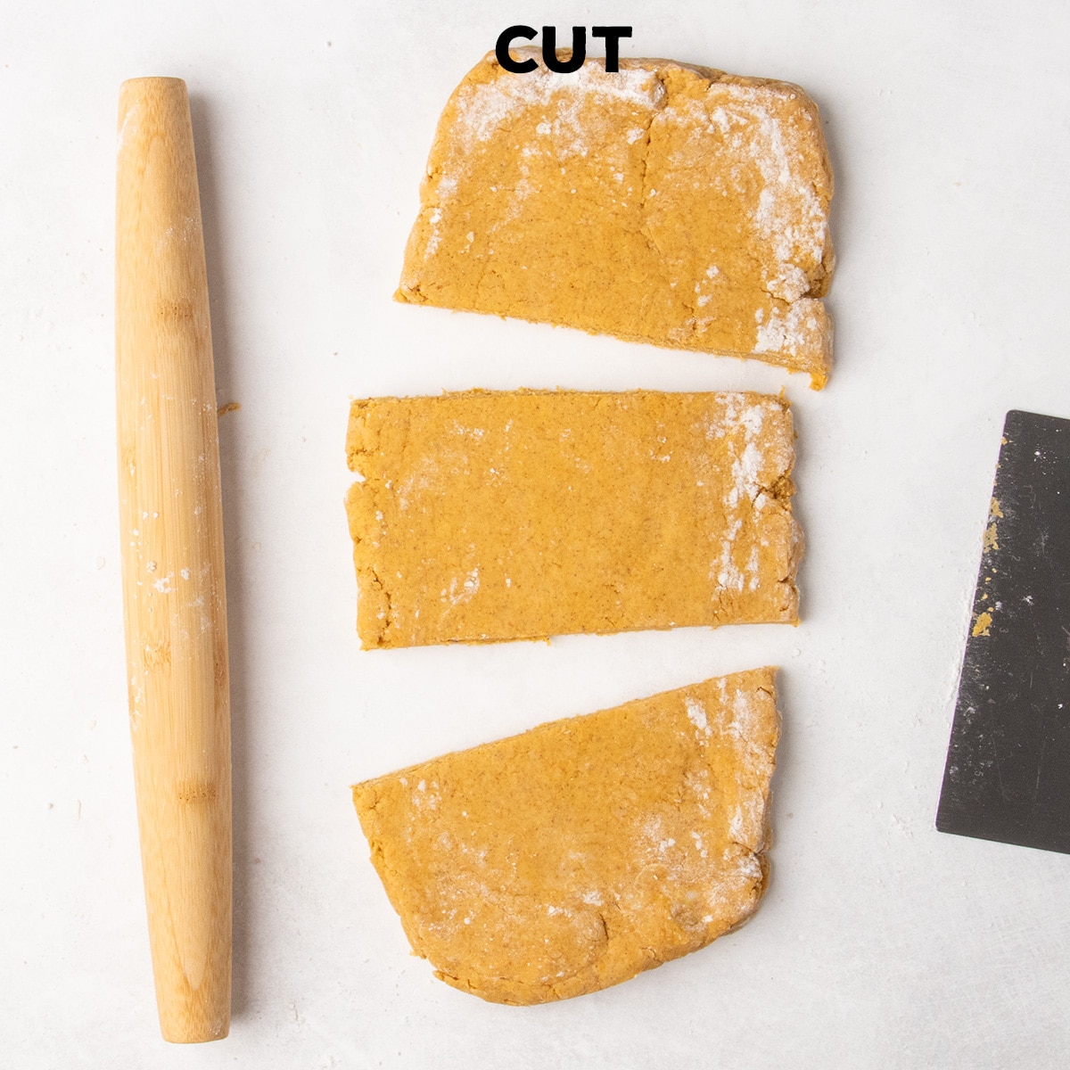 Rolled orange dough is cut crosswise into three sections beside a wooden rolling pin and metal bench scraper beneath the word “CUT.”
