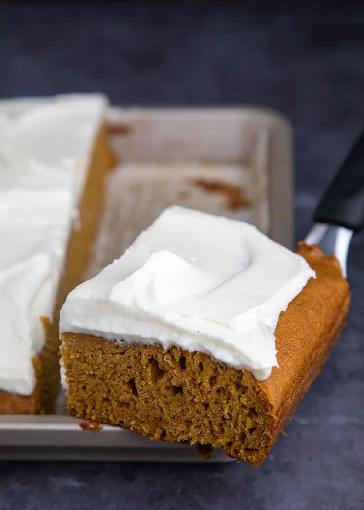 Frosted pumpkin square on spatula on edge of baking pan