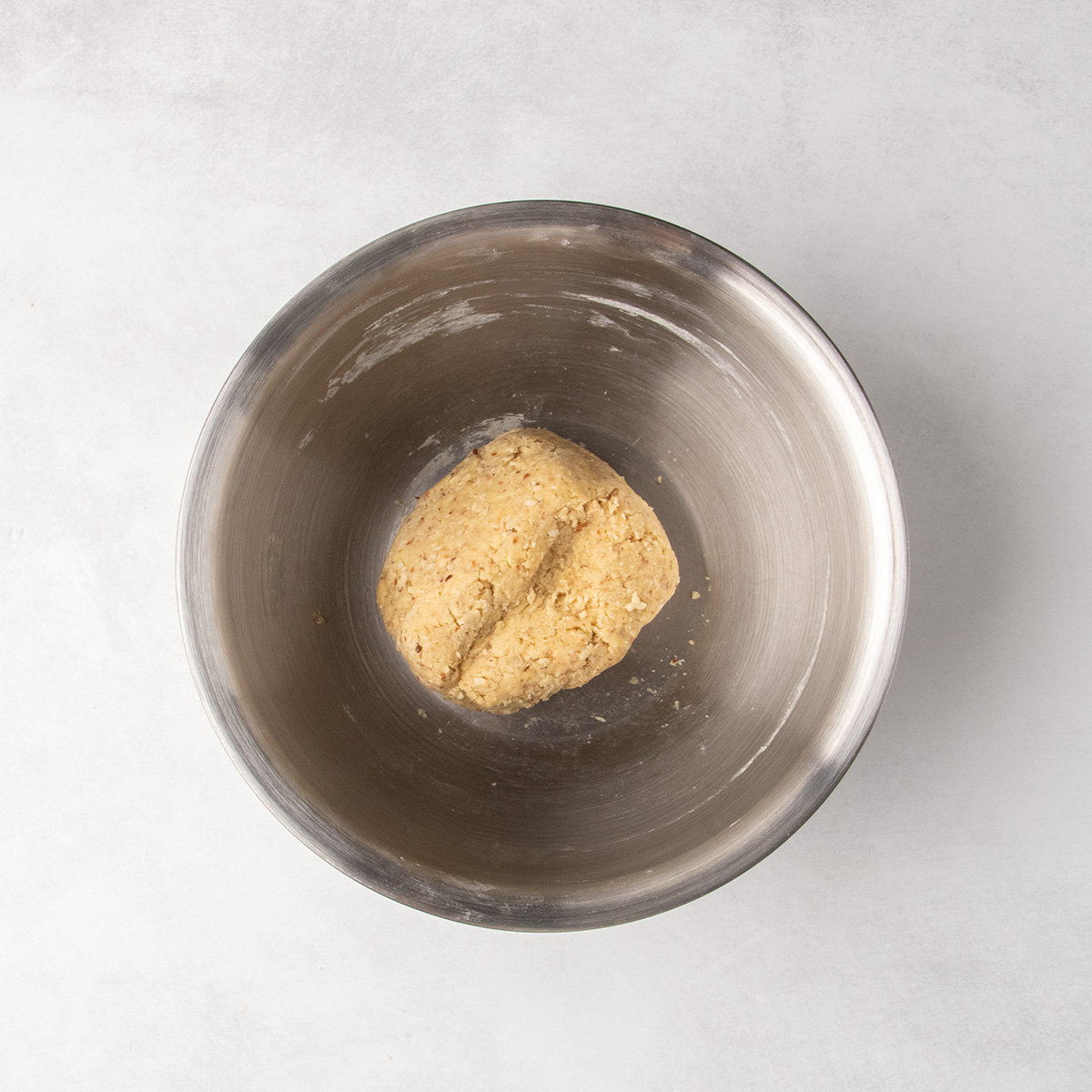 Pale speckled dough gathered into a compact mound in the center of a stainless steel mixing bowl.