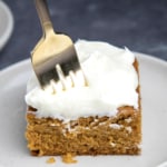Closeup image of fork piercing cream cheese frosting on top of gluten free pumpkin bar square on small white plate