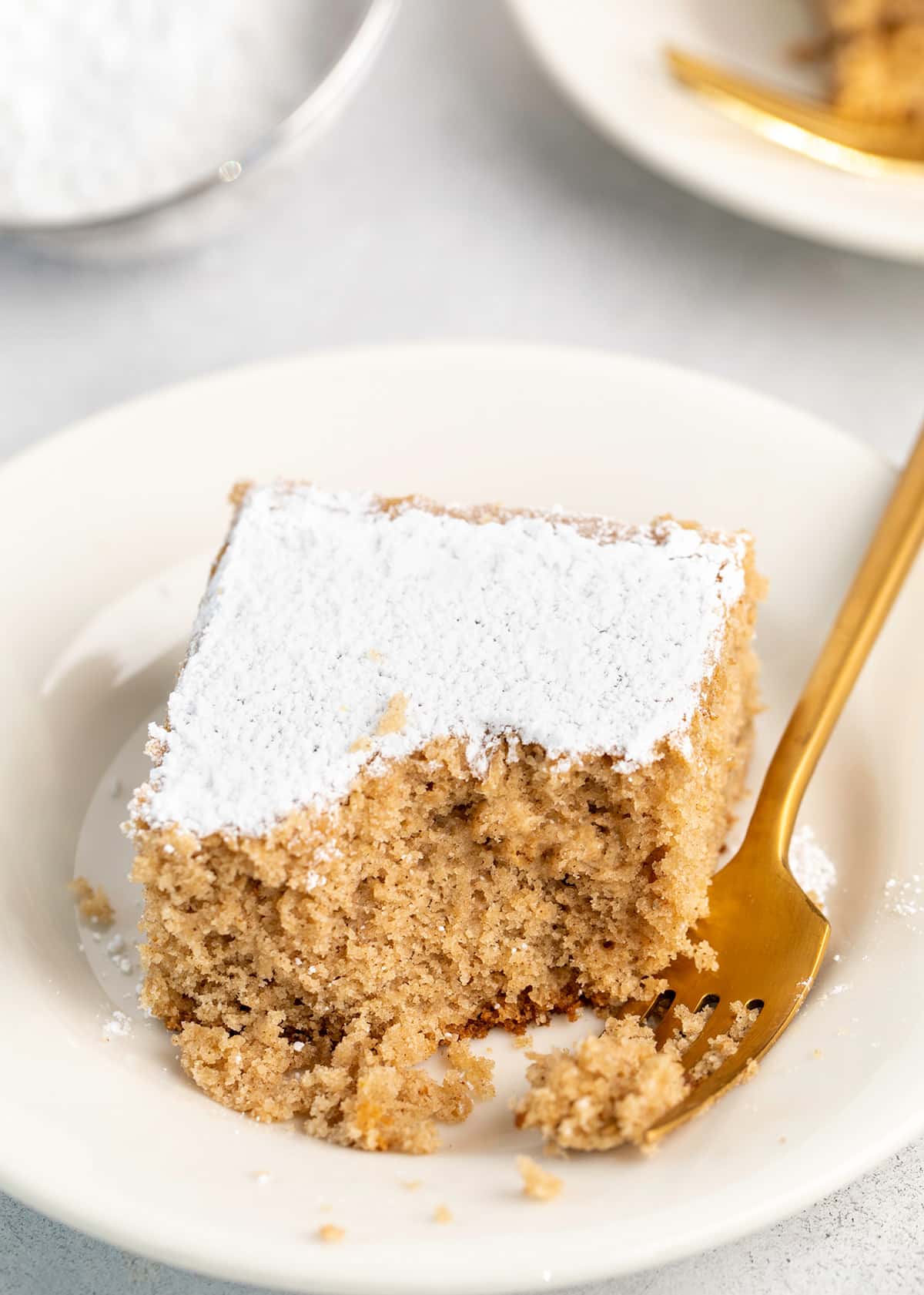 Piece of spice cake on small white plate with fork and bite taken