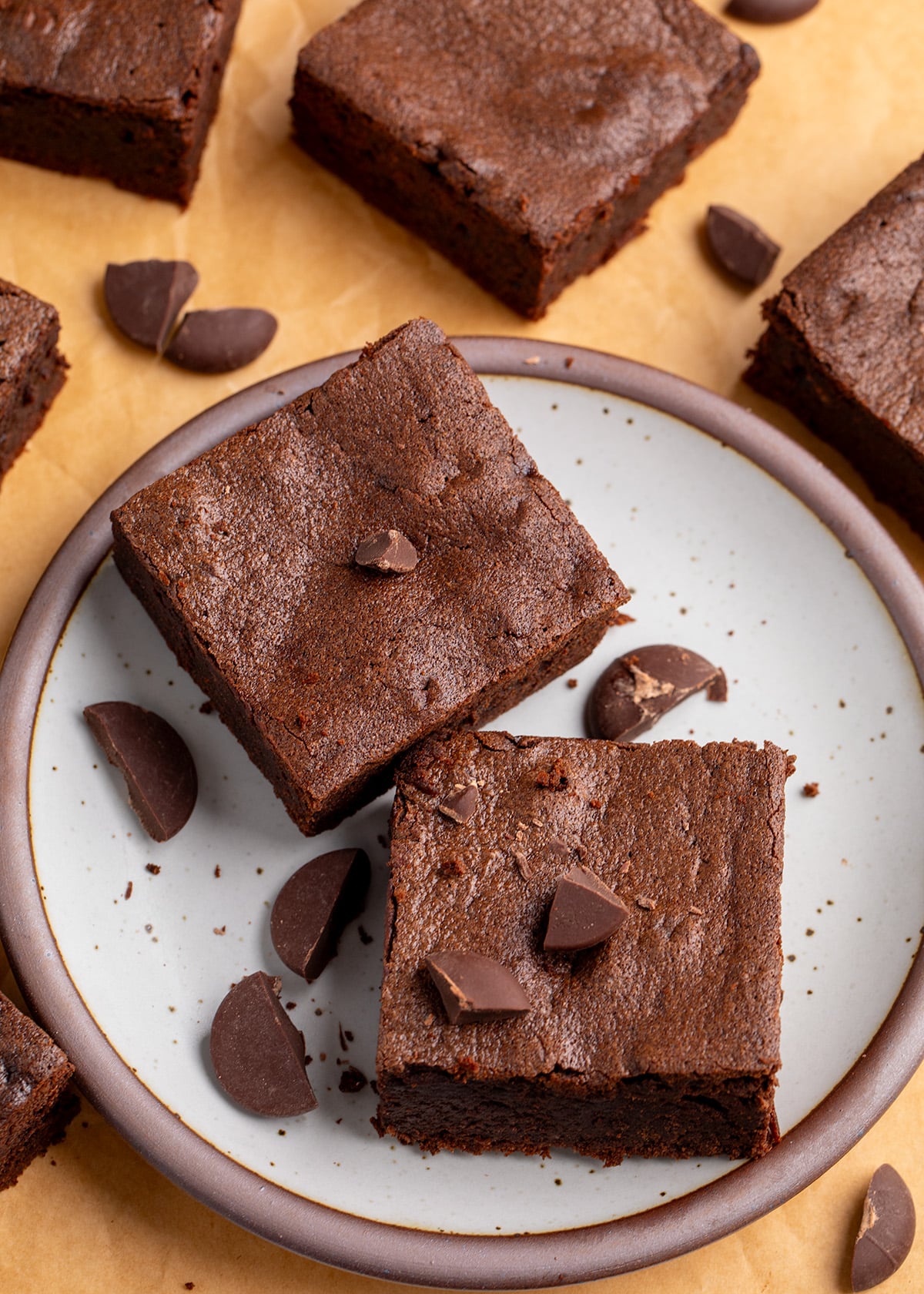 Overhead view of two thick chocolate brownies on a speckled plate with broken chocolate pieces scattered on and around them.