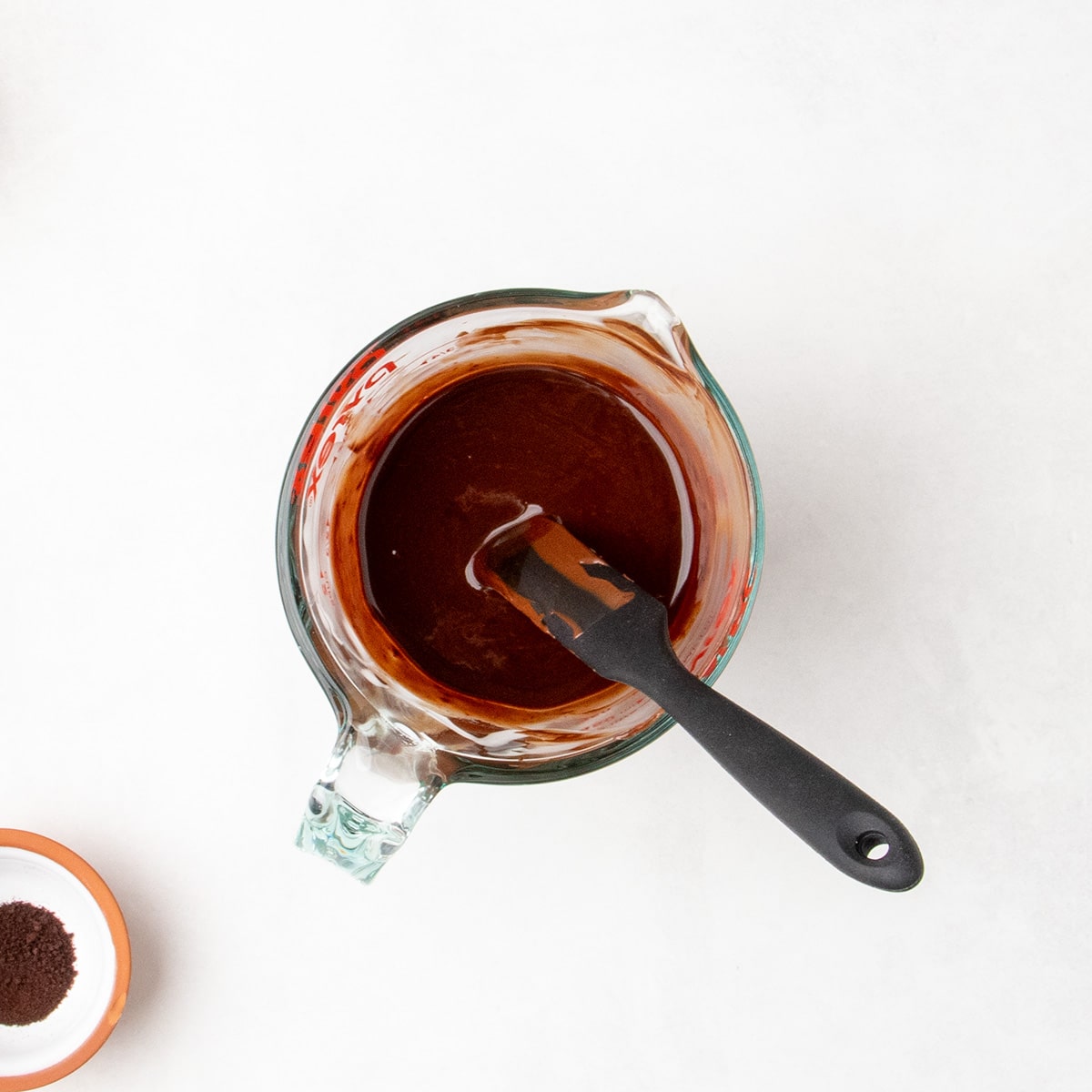 Overhead view of a glass measuring cup filled with smooth melted chocolate mixture and a black silicone spatula.