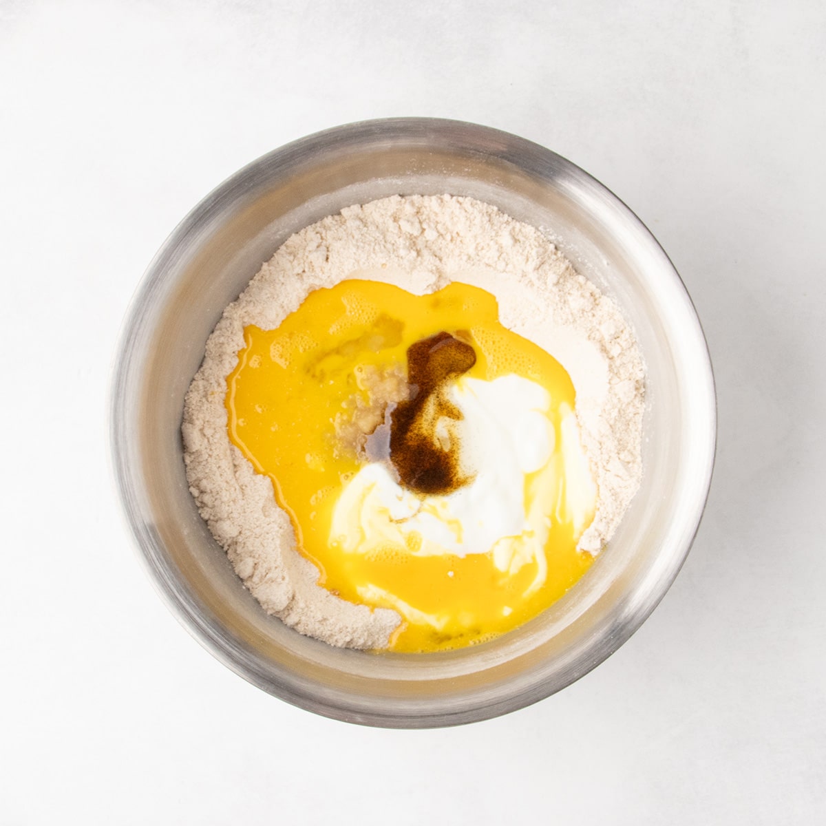 Same mixing bowl with white, brown and yellow wet ingredients added to the dry ingredients in a stainless steel mixing bowl.