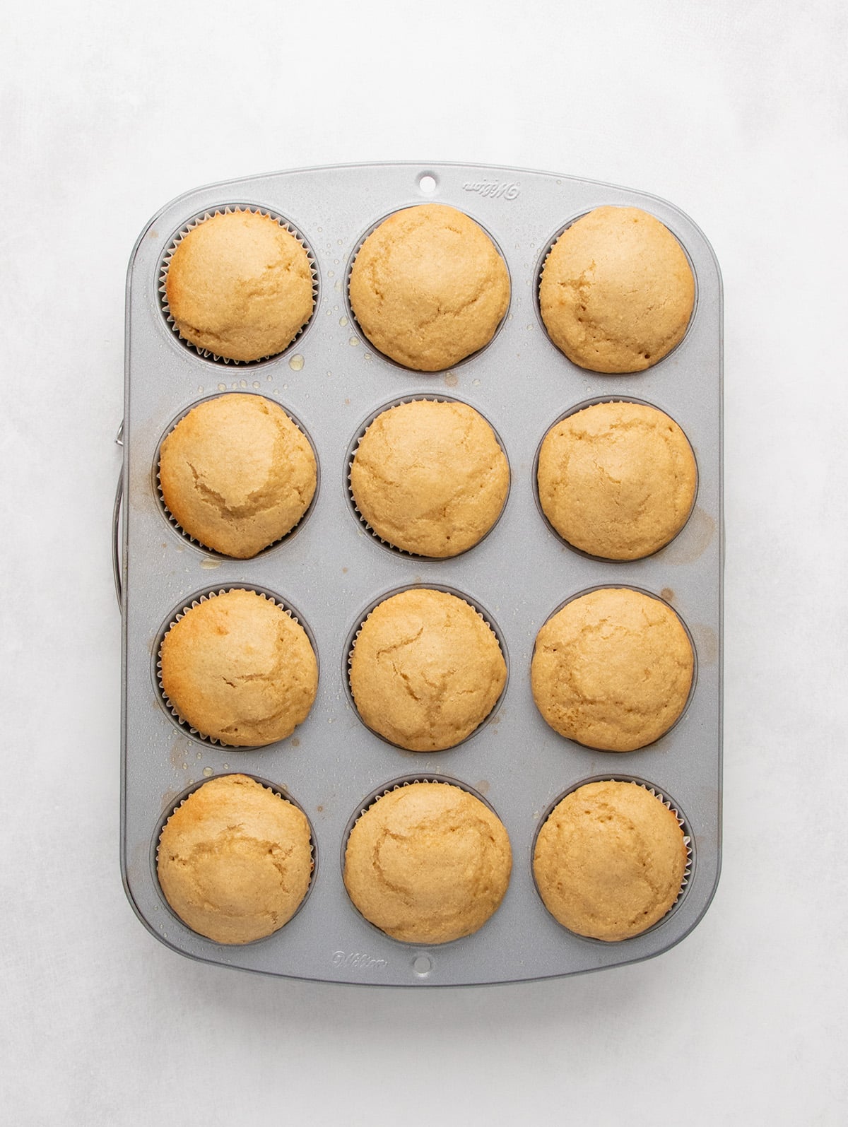 Brown baked protein muffins with round domes are shown in a 12-cup muffin tin from overhead.