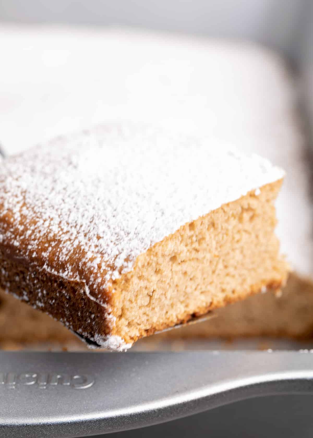 Square slice of spice cake with powdered sugar being lifted out of pan
